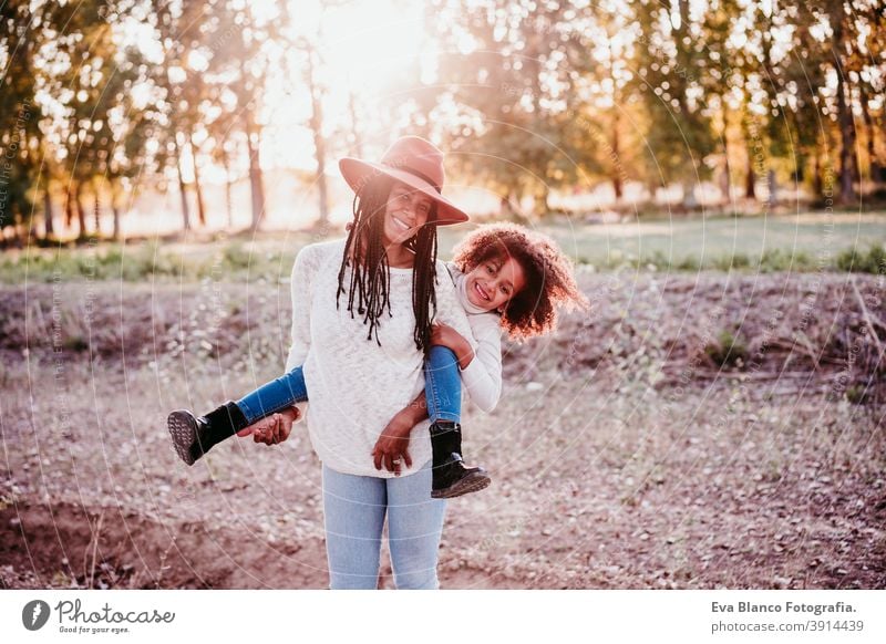 Porträt der hispanischen Mutter und afro Kind Mädchen spielen im Freien bei Sonnenuntergang während der goldenen Stunde. Herbstzeit. Familie Konzept Afro-Look