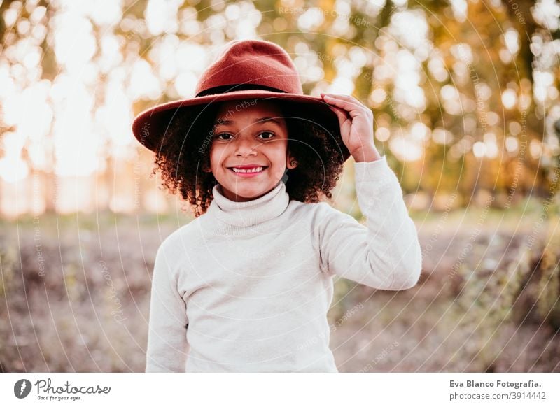 Porträt eines niedlichen Afro-Kindermädchens mit Hut bei Sonnenuntergang zur goldenen Stunde, Herbstzeit, schöne Bäume im Hintergrund Afro-Look Mädchen Natur