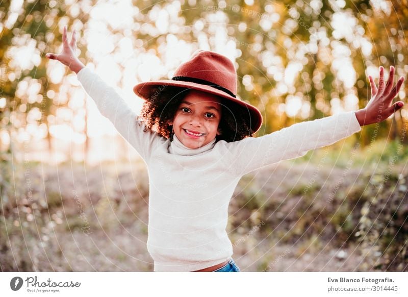 Porträt eines niedlichen Afro-Kindermädchens mit Hut bei Sonnenuntergang zur goldenen Stunde, Herbstzeit, schöne Bäume im Hintergrund Afro-Look Mädchen Natur