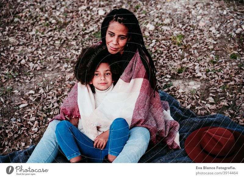 hispanische Mutter und afro Kind Mädchen im Freien umarmen bei Sonnenuntergang in Decke eingewickelt. Herbstzeit. Familie und Liebe Konzept Umarmung Afro-Look