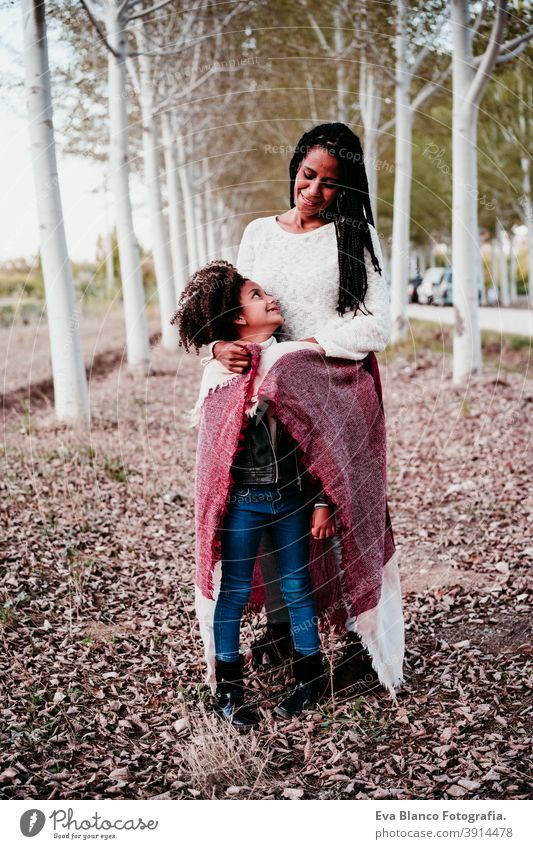 hispanische Mutter und afro Kind Mädchen im Freien umarmen bei Sonnenuntergang in Decke eingewickelt. Herbstzeit. Familie und Liebe Konzept Umarmung Afro-Look