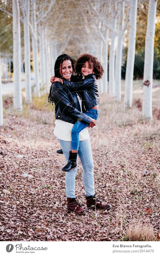 hispanische Mutter und afro Kind Mädchen im Freien umarmen bei Sonnenuntergang während der goldenen Stunde. Herbstzeit. Familie und Liebe Konzept Umarmung