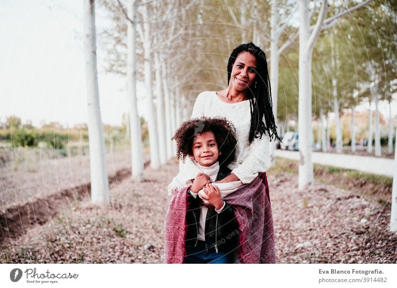 hispanische Mutter und afro Kind Mädchen im Freien umarmen bei Sonnenuntergang in Decke eingewickelt. Herbstzeit. Familie und Liebe Konzept Umarmung Afro-Look