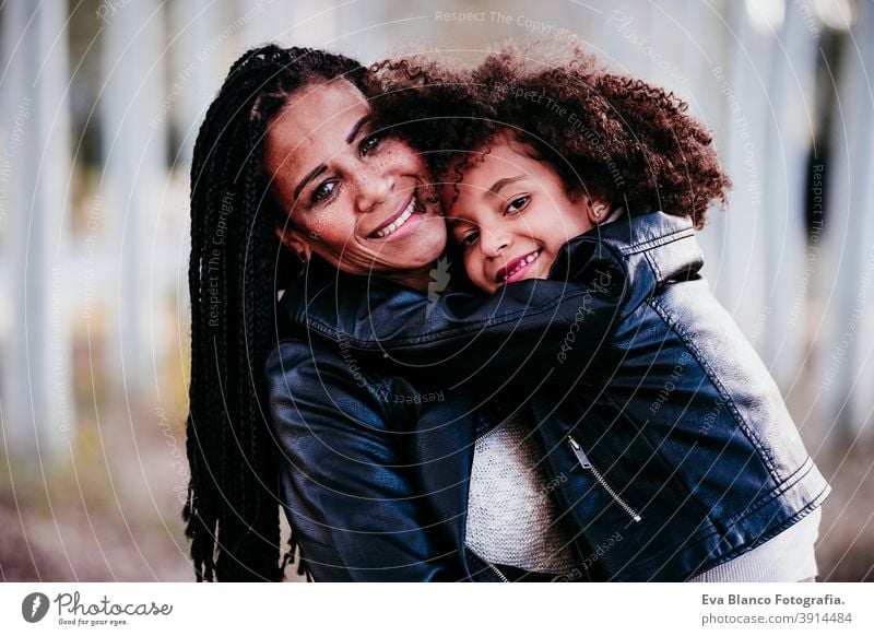 hispanische Mutter und afro Kind Mädchen im Freien umarmen bei Sonnenuntergang während der goldenen Stunde. Herbstzeit. Familie und Liebe Konzept Umarmung