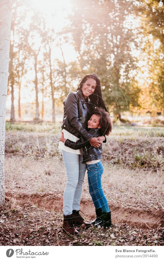 hispanische Mutter und afro Kind Mädchen im Freien umarmen bei Sonnenuntergang während der goldenen Stunde. Herbstzeit. Familie und Liebe Konzept Umarmung