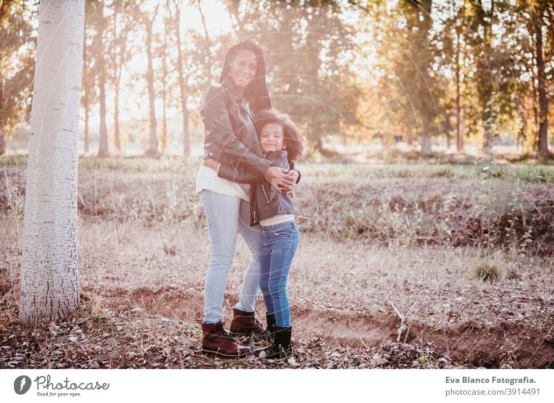 hispanische Mutter und afro Kind Mädchen im Freien umarmen bei Sonnenuntergang während der goldenen Stunde. Herbstzeit. Familie und Liebe Konzept Umarmung