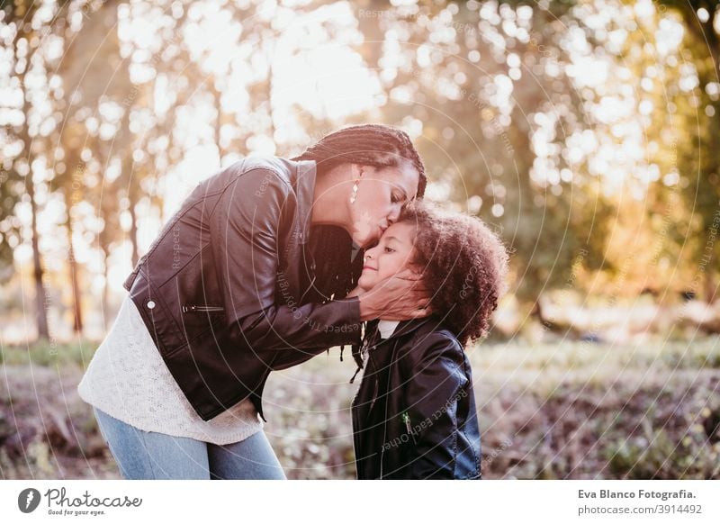 hispanische Mutter und afro Kind Mädchen im Freien umarmen bei Sonnenuntergang während der goldenen Stunde. Herbstzeit. Familie und Liebe Konzept Umarmung