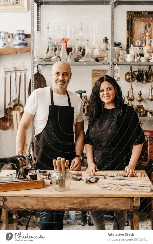 Fröhliches Kunsthandwerkerpaar an der Werkbank im Kunstatelier stehend Kunstgewerbler Paar Zimmerer Handwerk Zusammensein Werkstatt Arbeit Lächeln professionell