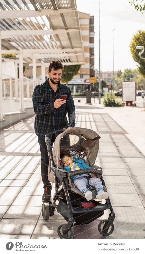 Bärtiger Mann mit seinem schlafenden Baby auf Auto schauen Telefon Vater Spaziergang Kleinwagen Männer männlich 40s Erwachsener attraktiv Herbst Vollbart bärtig