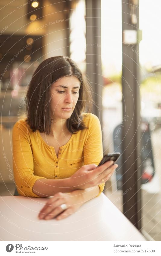 Frau in Bar in der Nähe von Fenster suchen Smartphone Telefon Blick hübsch Restaurant 30s ernst lesen Frauen Hinweise im Innenbereich Gelassenheit Nachrichten