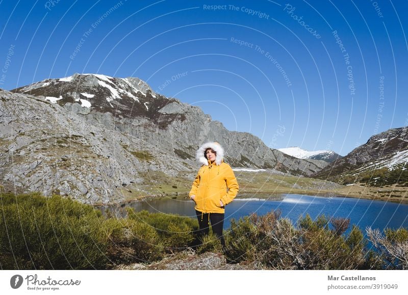 Berglandschaft mit verschneiten Bergen und See. Frau in gelber Jacke schaut in die Kamera. Aussehen gestellt kalt gelbe Jacke Wasser Landschaft Berge u. Gebirge