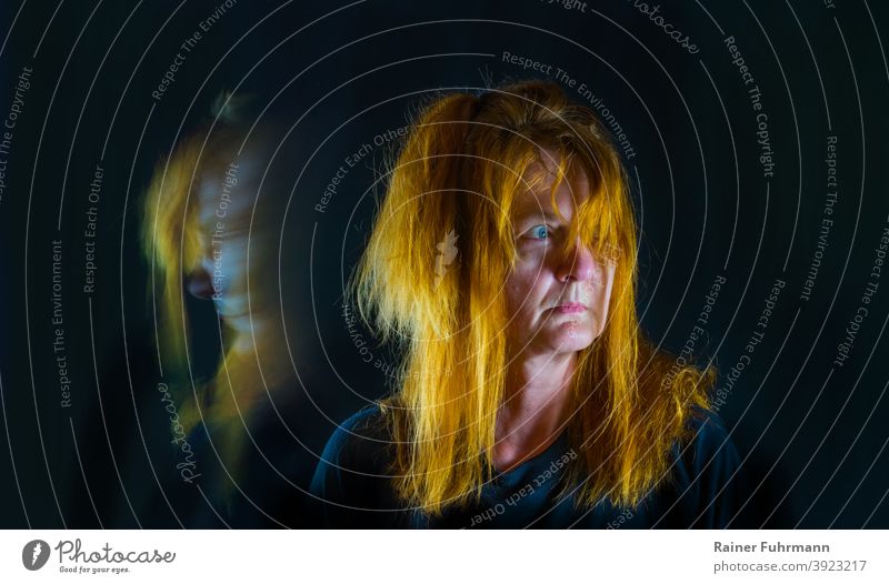 Eine Frau mit roten Haaren steht in der Dunkelheit. Sie blickt panisch in ein Licht. Porträt Panik schwarz Blick Schatten Angst Gesicht dunkel Nacht bedrohlich