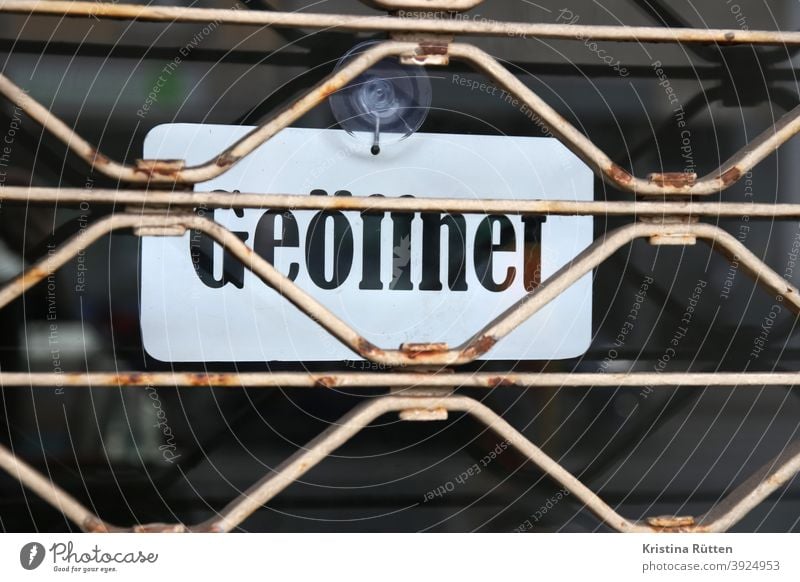 geöffnet schild hinter geschlossenem rollgitter aushang verschlossen zu widersprüchlich widerspruch tür eingang öffnungszeiten geschäftszeiten business laden