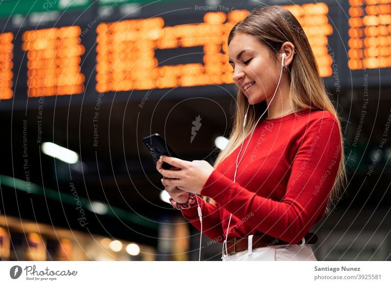 Mädchen im Bahnhof Station Seitenansicht Blick auf das Telefon Kopfhörer Porträt jung 20s blond hübsch per Telefon Funktelefon Kaukasier Stehen Frau Smartphone