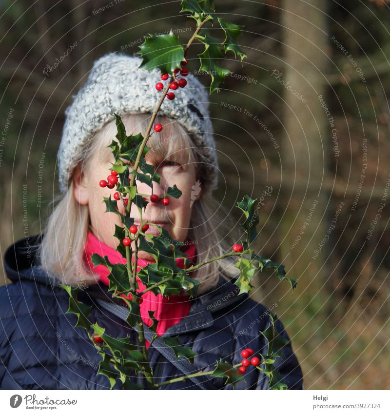 inkognito ;-) - Porträt einer Seniorin mit langem Haar und Mütze, die sich hinter einem Stechpalmenzweig versteckt Mensch Frau grauhaarig Mantel Ilex Zweig