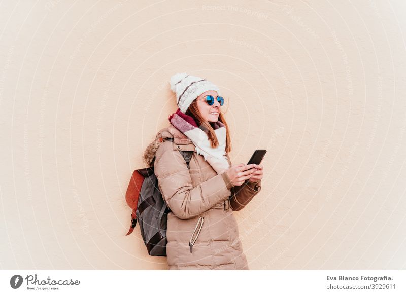 Frau mit Mobiltelefon über gelbe Wand Hintergrund. Technologie und Winter Konzept im Freien Großstadt Handy Technik & Technologie Lebensstile Sonnenbrille