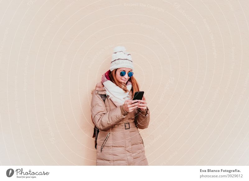 Frau mit Mobiltelefon über gelbe Wand Hintergrund. Technologie und Winter Konzept im Freien Großstadt Handy Technik & Technologie Lebensstile Sonnenbrille