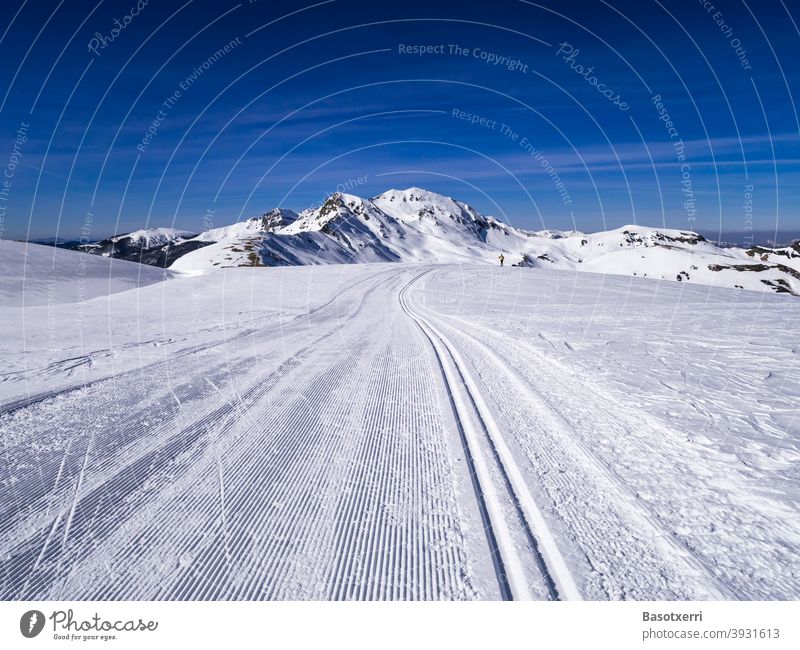 Gespurte Skilanglaufpiste in den Bergen. Kleine Person (Skilangläuferin) im Hintergrund. Isaba/Belagua, Navarra in den spanischen Pyrenäen. Skipiste Spur