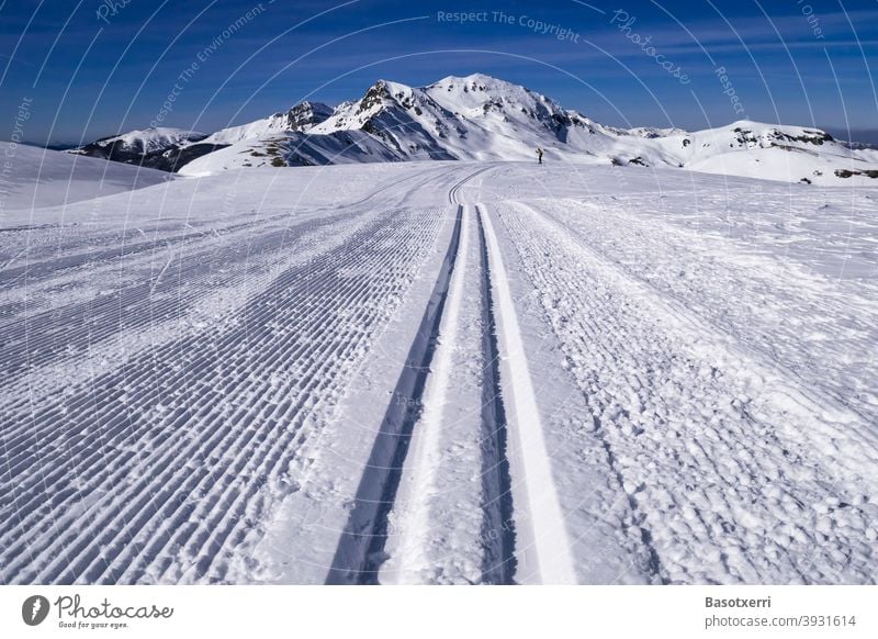 Gespurte Skilanglaufpiste in den Bergen. Kleine Person (Skilangläuferin) im Hintergrund. Isaba/Belagua, Navarra in den spanischen Pyrenäen. Skipiste Spur