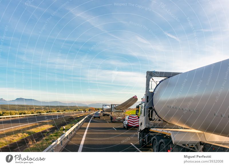 Sondertransport von Windradflügeln. Mehrere LKWs mit Windradflügeln, die auf der Autobahn zirkulieren, mit Bakenfahrzeugen dahinter, um andere Verkehrsteilnehmer vor der Gefahr zu warnen.