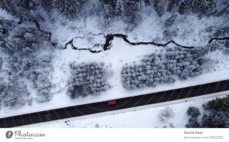 Luftaufnahme mit einer Drohne von einer Straße mit einem Auto das im Winter durch den Wald fährt luftaufnahme drohnenfoto auto winter straße fahren schnee wald