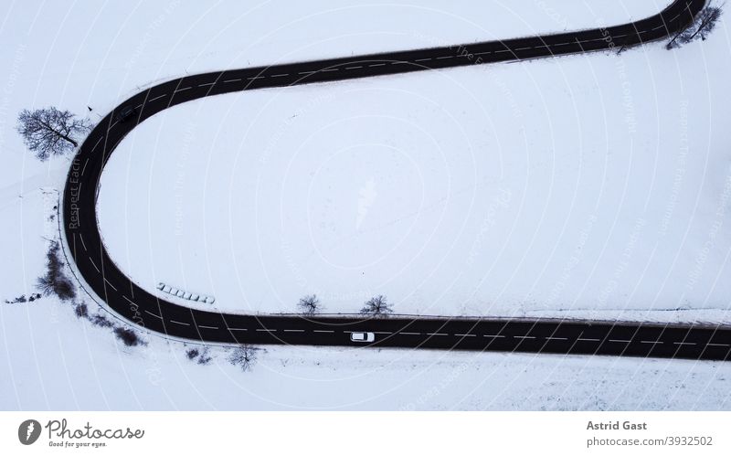 Luftaufnahme mit einer Drohne von einer Straßenkurve mit einem fahrenden Auto im Winter luftaufnahme drohnenfoto auto winter straße schnee kehre straßenkurve