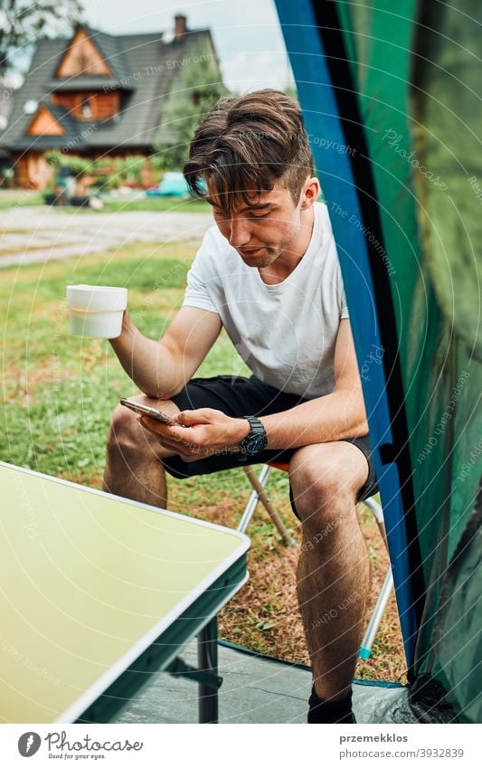 Junger Mann trinkt einen Kaffee sitzend vor dem Zelt am Morgen Abenteuer Getränk Pause Frühstück Lager Camping Nahaufnahme Tasse trinken Erkundung Freiheit