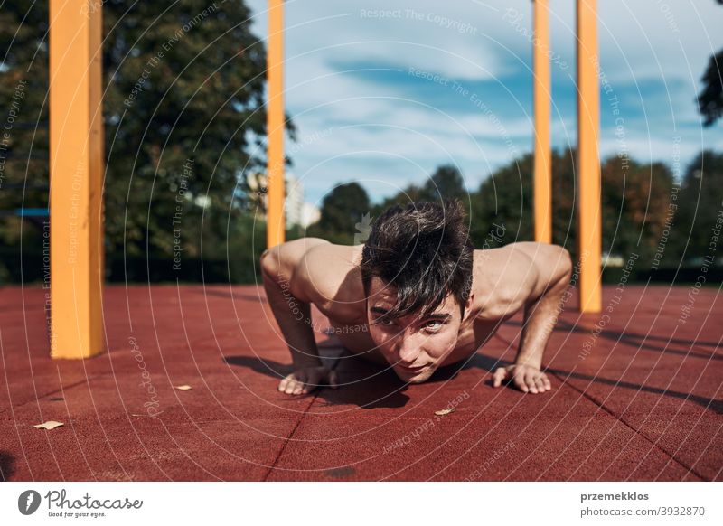 Junger hemdloser Bodybuilder macht Liegestützen auf rotem Gummiboden während seines Trainings in einem modernen Gymnastikpark calisthenics Pflege Kaukasier