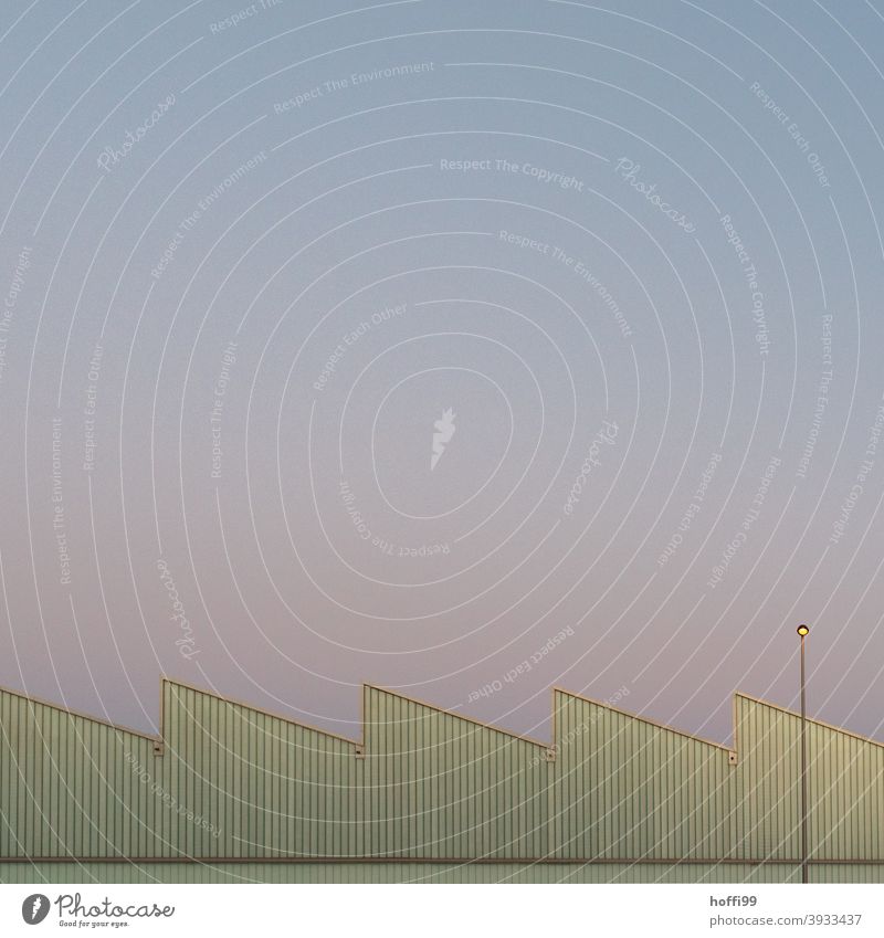 Lindgrüne Zickzack Fassade mit Lampe vor winterlichem Abendhimmel beim Sonnenuntergang Industriefotografie Lagerhalle Winterlicht Sonnenuntergangslicht