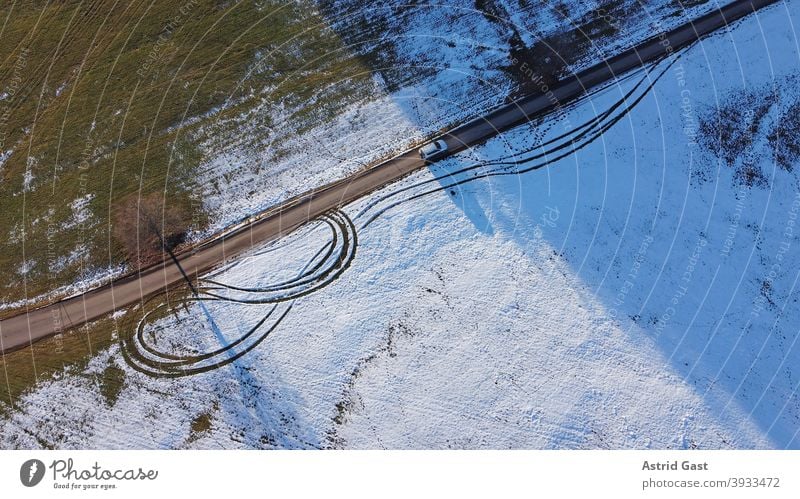 Drohnenfoto von einem weißen Auto, das im Winter auf einer Straße vom Licht in den Schatten fährt luftaufnahme drohnenfoto auto winter straße fahren schnee