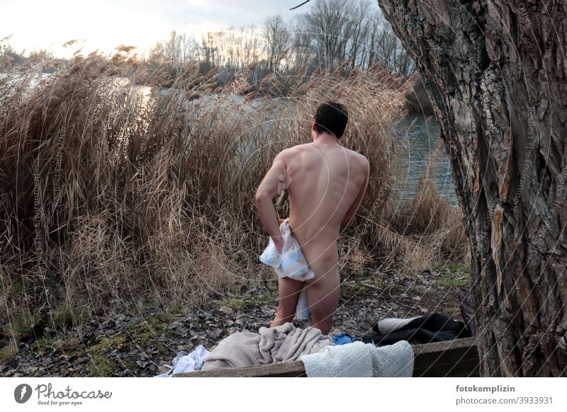 Rückenansicht eines nackten jungen Mannes, der sich nach einem kalten Bad im Winter abtrocknet Eisschwimmen nackter Mann eisbaden abhärten Abhärtung