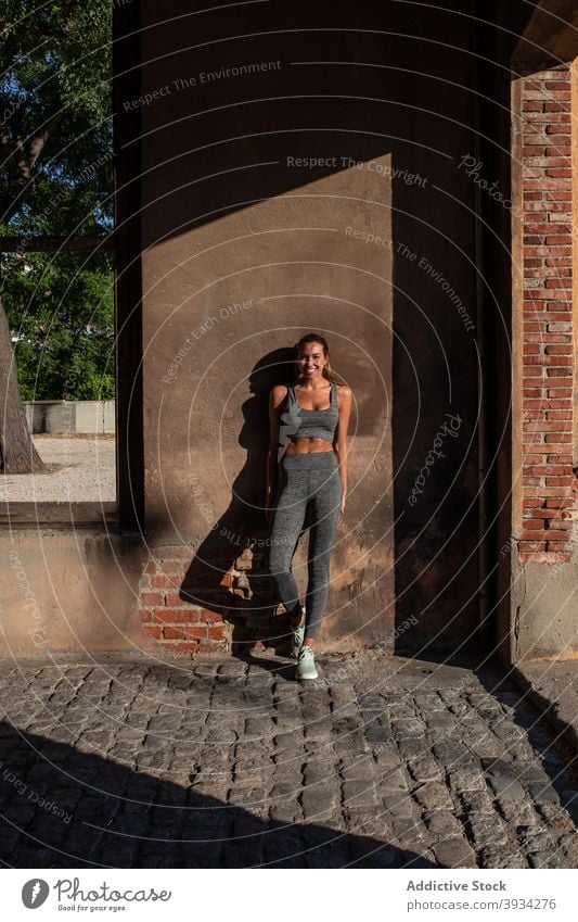 Schlanke Sportlerin steht in der Nähe von Gebäude auf der Straße passen schlank Athlet Läufer Großstadt heiter Sportkleidung Sommer Frau Wand schäbig