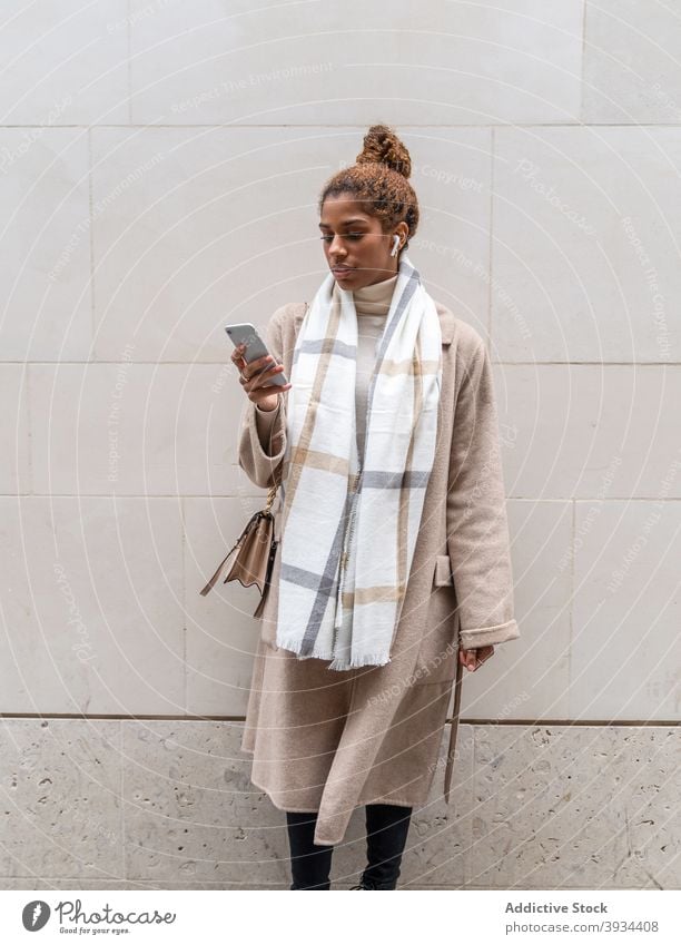 Stilvolle junge ethnische Frau Messaging auf Smartphone beim Gehen auf der Straße Spaziergang benutzend Unternehmer Arbeit Nachricht Laptop Großstadt Browsen