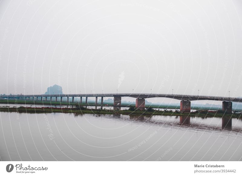 Filmische Szenerie einer Brücke über den Fluss an einem dunklen und stimmungsvollen Tag in Ninh Binh Vietnam Einsamkeit Windstille Reisefotografie