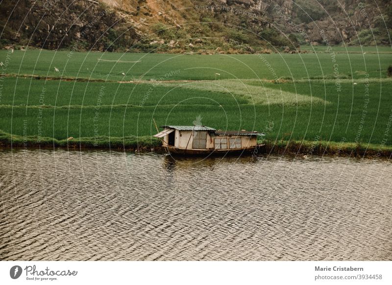 Filmische Szenerie eines hölzernen Bootshauses, das am Flussufer von Ninh Binh, Vietnam, vertäut ist filmisch Ländliche Szene Ackerbau Reisfeld fliegend Provinz