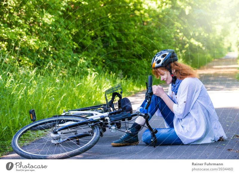 eine Frau hatte einen Unfall, sie ist mit einem Fahrrad gestürzt und hat sich verletzt Fahrradunfall Sturz Verletzung Fahrradfahrer Helm Knie Strasse Weg Sommer