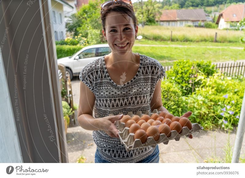 Lieferung von frischen Eiern an der Haustür durch eine junge lächelnde Frau. im Innenbereich Versand heimwärts Saison Dienst Ladung Arbeit Karton Kunde