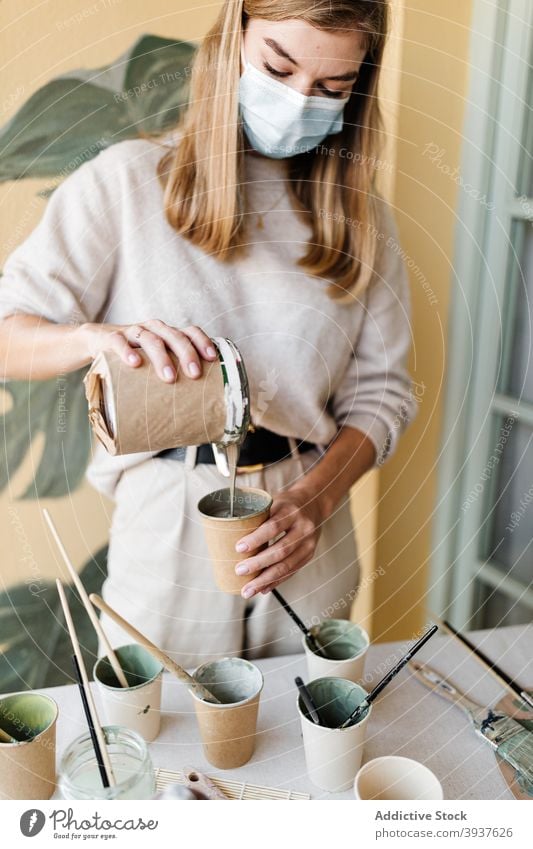 Frau mischen Farben für die Erstellung von Gemälde an der Wand Künstler Anstreicher heimwärts Pigment eingießen Fensterblätter Blatt Mundschutz behüten Tasse