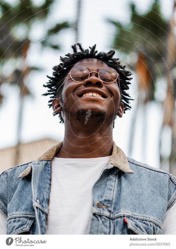 Optimistischer schwarzer Mann in trendigem Outfit und Brille heiter Glück trendy Afro-Look Rastalocken Stil jung charismatisch männlich Afroamerikaner ethnisch