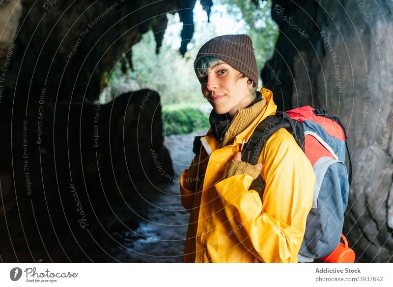 Erfreute Entdeckerin mit Rucksack schaut in die Kamera Reisender Frau heiter Durchgang Bogen felsig Oberbekleidung Herbst Urlaub Cobijero-Strand Asturien