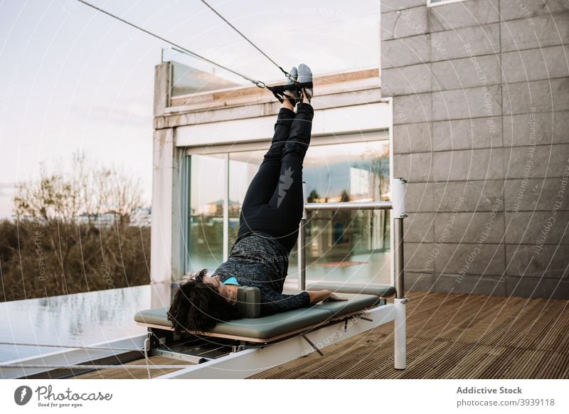 Ruhige Frau macht Yoga in Supported Shoulder Stand Pose auf Pilates-Maschine Asana Reformer Übung Gleichgewicht unterstützte Schulterstand-Pose Gurt Dehnung