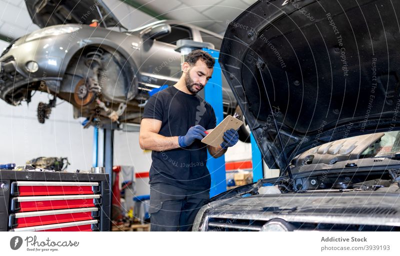 Männlicher Mechaniker mit Diagramm auf Zwischenablage im Autoservice untersuchen PKW Mann Techniker Tabelle Diagnostik Analyse männlich modern Automobil