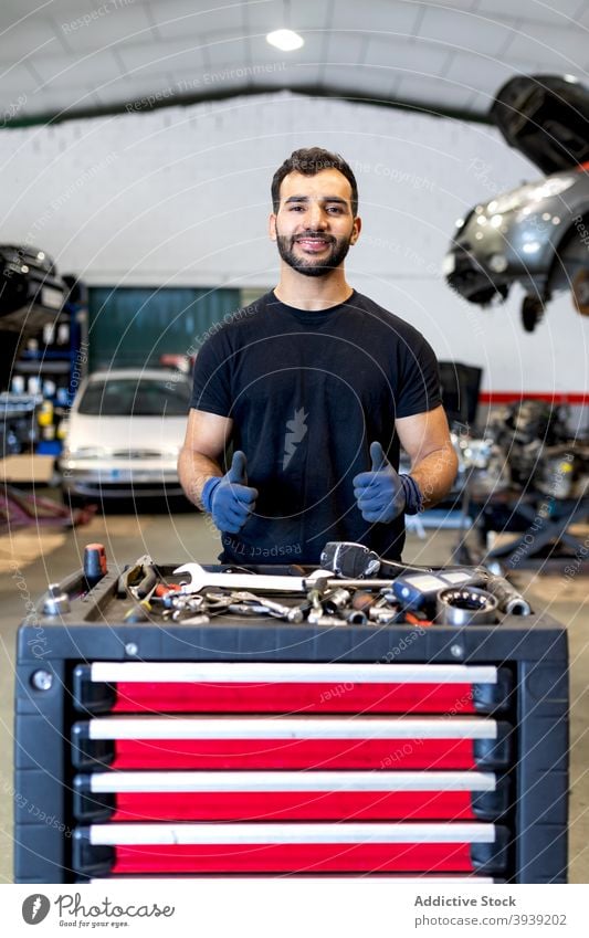 Lächelnder Mann mit Werkzeugschrank im Autoservice Kabinett PKW Mechaniker Techniker Dienst Instrument Daumen hoch gestikulieren männlich verschiedene Glück Job