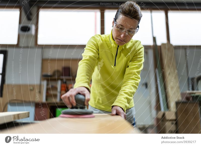 Konzentrierte Frau glättet Holz mit Schleifmaschine polnisch hölzern Schiffsplanken Maschine Tischlerarbeit professionell Meister Zimmerer Fähigkeit Orbital