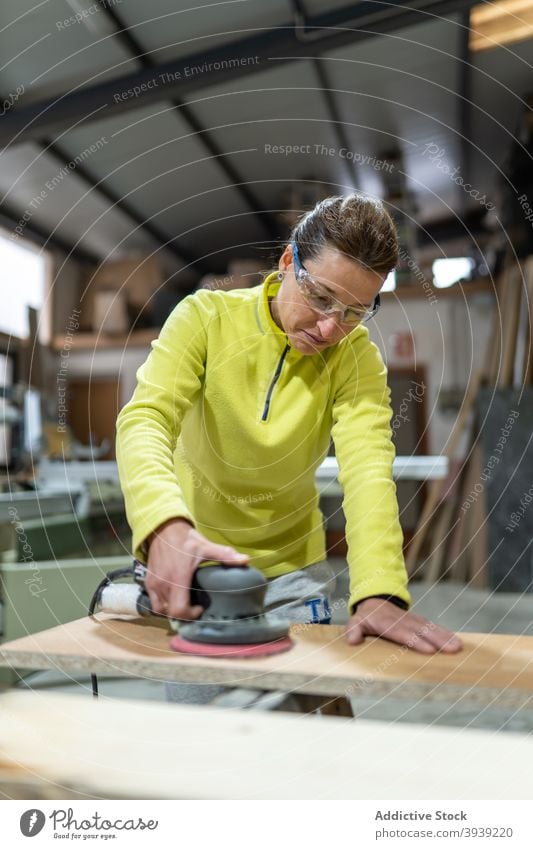 Konzentrierte Frau glättet Holz mit Schleifmaschine polnisch hölzern Schiffsplanken Maschine Tischlerarbeit professionell Meister Zimmerer Fähigkeit Orbital