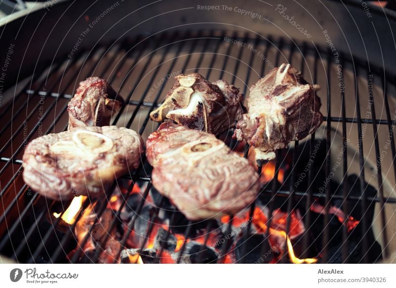 Mehrere Beinscheiben und Rinderknochen fertig gegrillt auf einem Kamado- Grill auf dem Grillrost Keramischer Grill Kamado Grill grün heiß Ruß Rust Töpferwaren