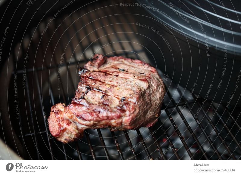 Ein Stück fertiges Roastbeef mit Grillstreifen auf einem Kamado- Grill neben einem Bräter Grillrost Holzkohle-Glut Keramischer Grill Kamado Grill grün heiß Ruß