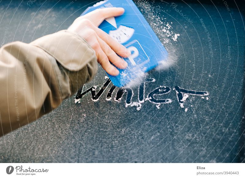 Hand kratzt mit einem Eiskratzer die vereiste Autoscheibe frei auf der das Wort Winter steht Frost kratzen Scheibe gefroren PKW Autofenster Windschutzscheibe