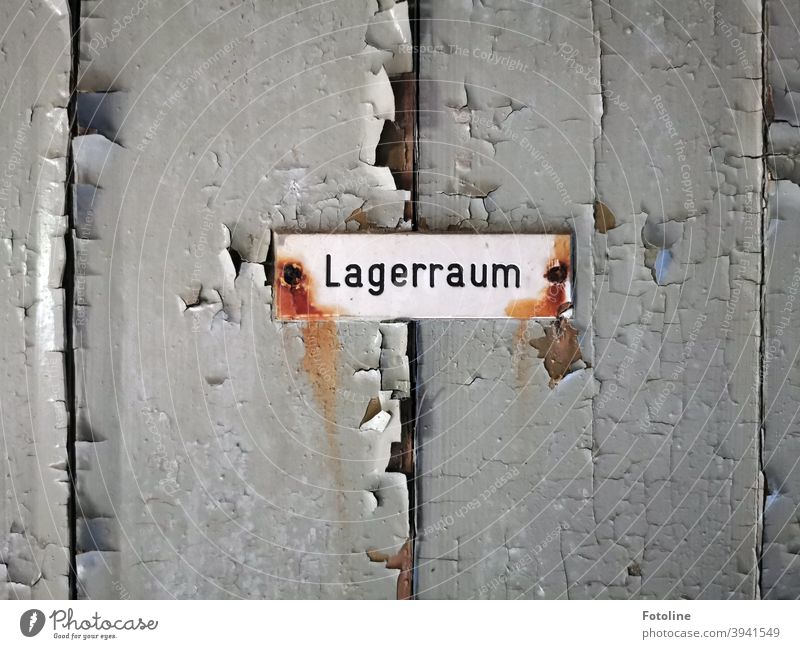 Lagerraum - oder eine alte Holztür bei der der Putz abblättert mit einem verrosteten angeschraubten Schild, auf dem Lagerraum steht. Lost Place kaputt verlassen