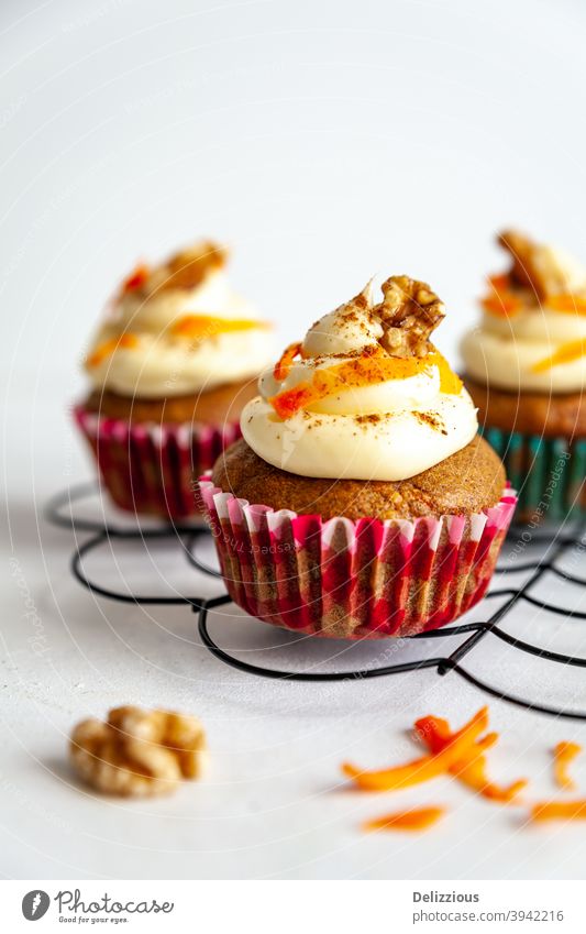 drei Karottenkuchen Muffin mit Zuckerguss und Karotte Rasur auf Kühlregal weißem Hintergrund Cupcake Kuchen Dessert Lebensmittel süß gebacken Zuckerguß